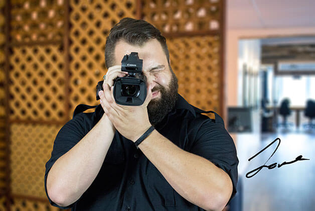 Headshot of Dave Adams holding video camera with his signature
